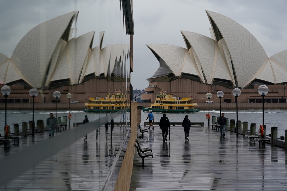 People walk in wet conditions along the waterfront near the Sydney Opera House as eastern Australia experiences a winter cold front, in Sydney, Australia, June 10, 2021. REUTERS/Loren Elliott
