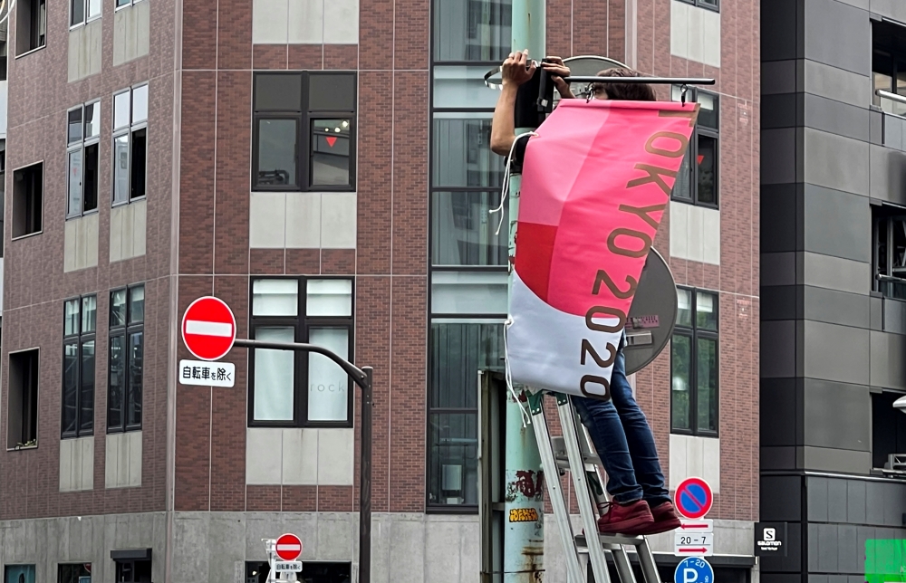 A worker attaches a Tokyo 2020 Olympic Games banner on a lamp post in Tokyo, Japan, June 16, 2021. (Reuters/Pawel Kopczynski)