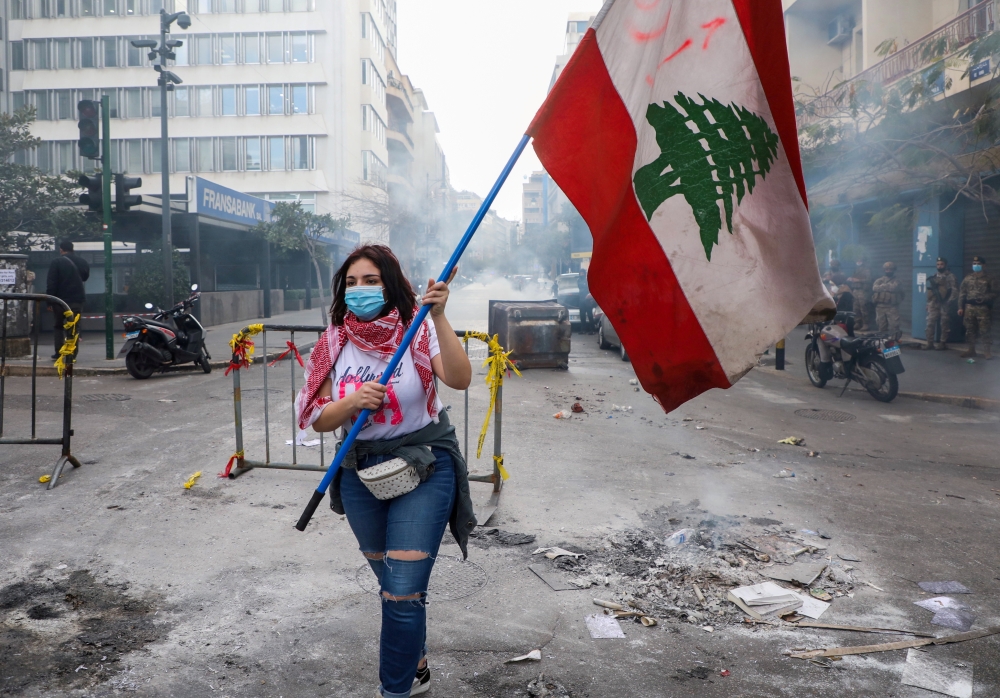 FILE PHOTO: A demonstrator carries a national flag along a blocked road, during a protest against the fall in Lebanese pound currency and mounting economic hardships, near the Central Bank building, in Beirut, Lebanon March 16, 2021. REUTERS/Mohamed Azaki