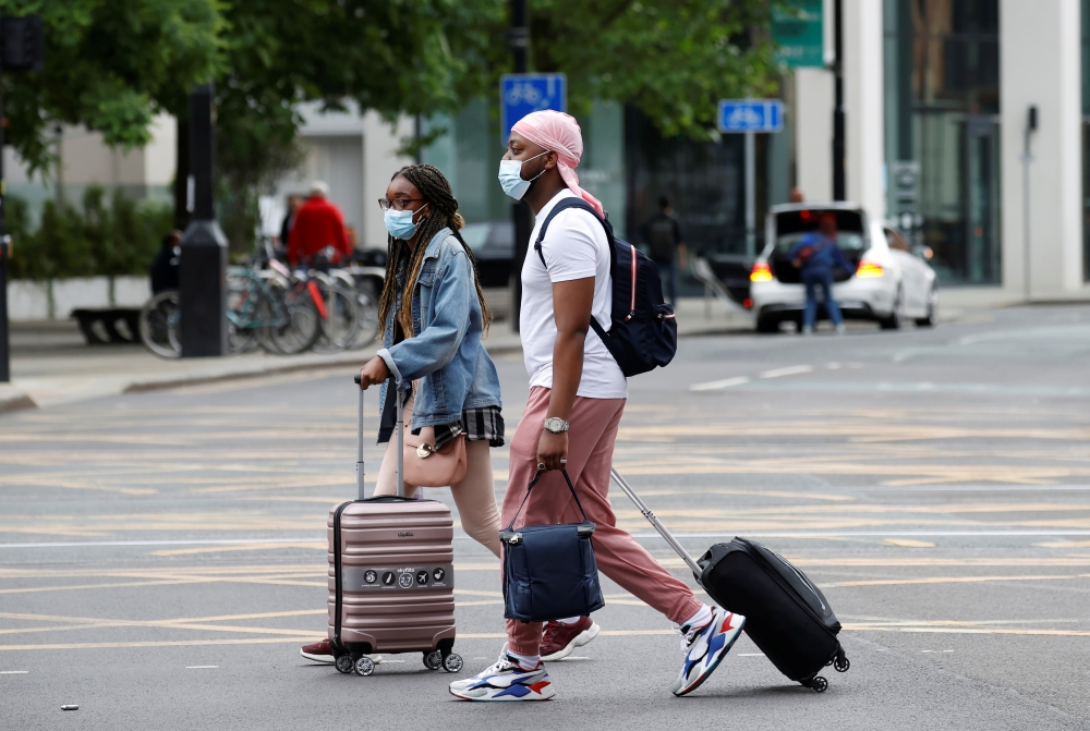 People wear protective masks as they walk with suitcases through the city centre, amid the outbreak of the coronavirus disease (COVID-19) in Manchester, Britain, June 21, 2021. REUTERS/Phil Noble