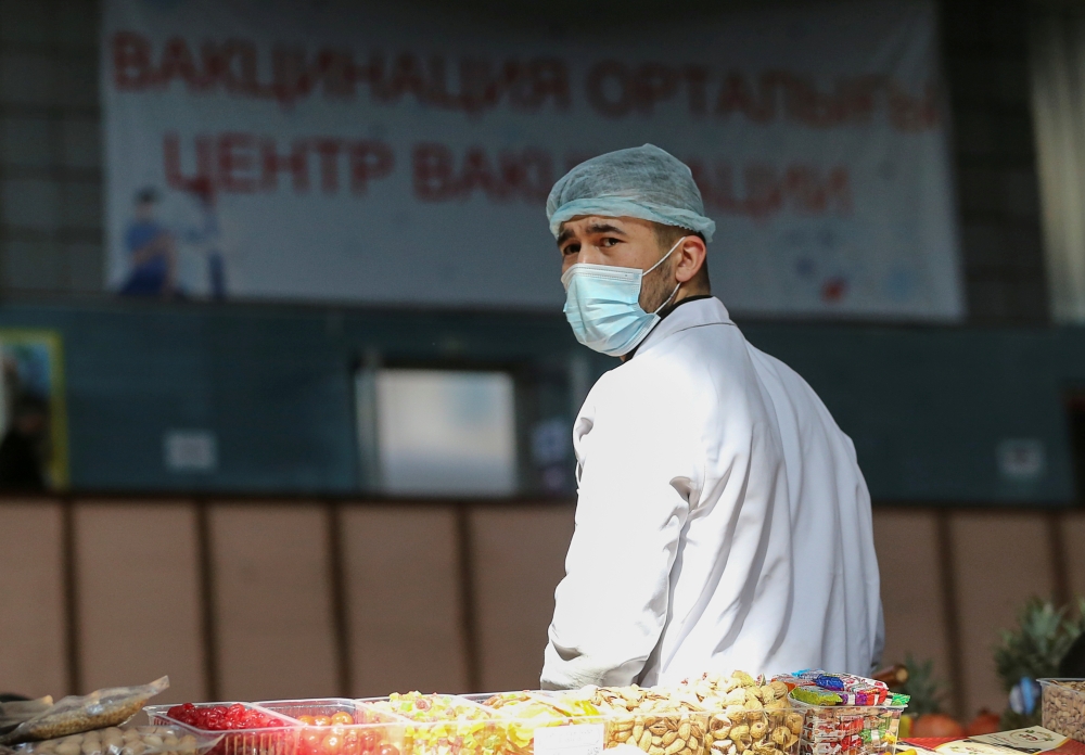 A vendor wearing a protective face mask waits for customers near an information banner placed outside the coronavirus disease (COVID-19) vaccination centre at a food market in Almaty, Kazakhstan April 14, 2021. Picture taken April 14, 2021. REUTERS/Pavel 