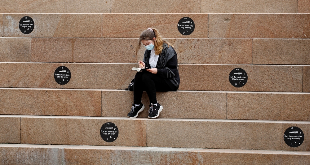 A woman wears a protective mask as she reads a book amongst social distancing markers, amid the outbreak of the coronavirus disease (COVID-19) in Liverpool, Britain, June 28, 2021. REUTERS/Phil Noble