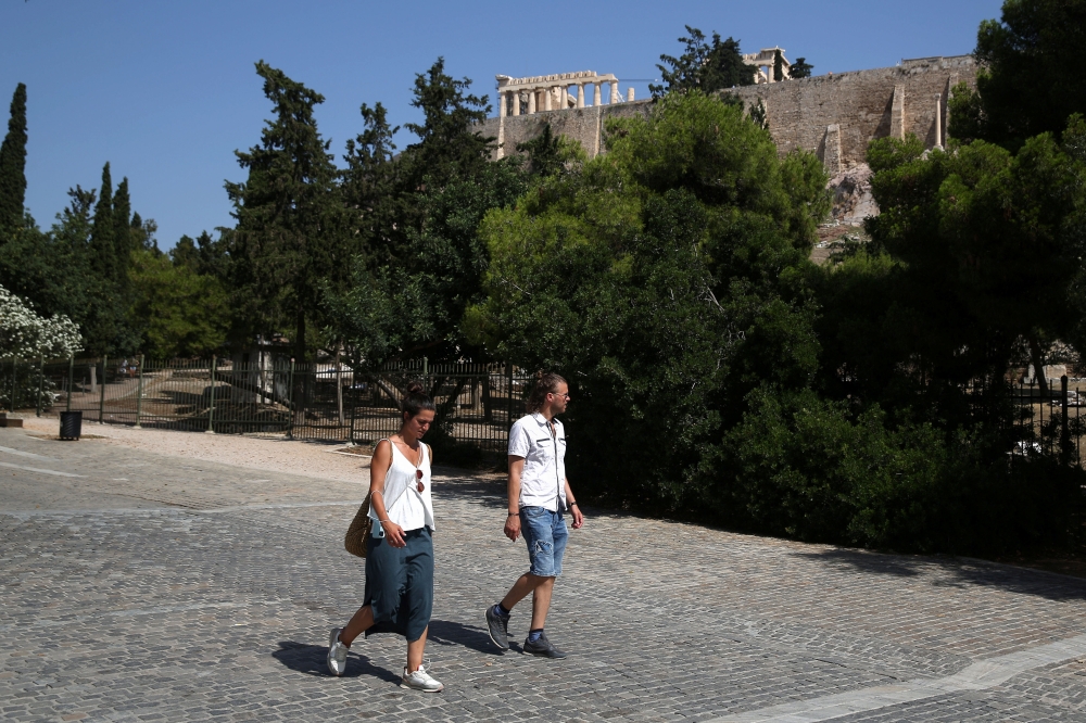 People without protective face masks make their way on the Areopagitou pedestrian street, as the ancient Parthenon temple is seen atop the Acropolis hill, following the easing of measures against the spread of the coronavirus disease (COVID-19) in Athens,