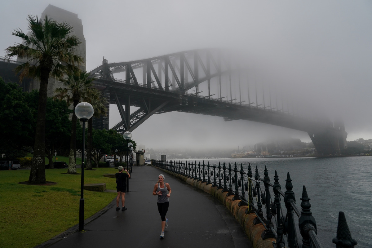 A woman jogs along the waterfront past the Sydney Harbour Bridge, seen shrouded in fog, during a lockdown to curb the spread of a coronavirus disease (COVID-19) outbreak in Sydney, Australia, June 30, 2021. REUTERS/Loren Elliott
