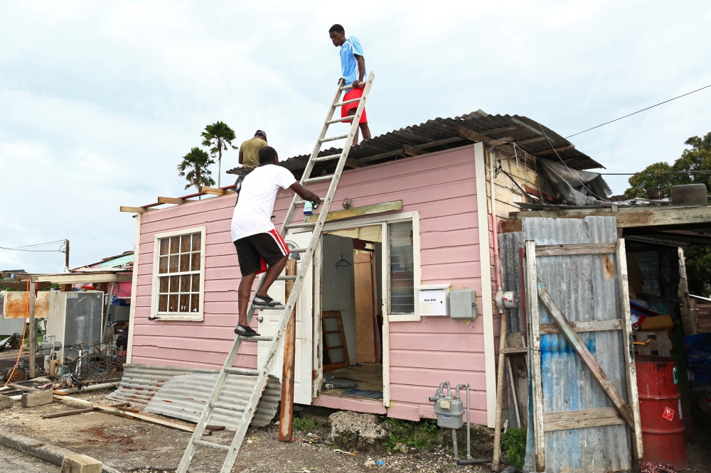 Men fix the roof of a house after strong winds of Hurricane Elsa passed St. Michael, Barbados July 2, 2021. (Reuters/Nigel Browne)