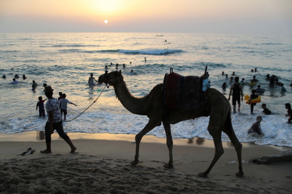 A man walks by with a camel as Palestinians spend time at a beach in Gaza July 2, 2021. (Reuters/Mohammed Salem)