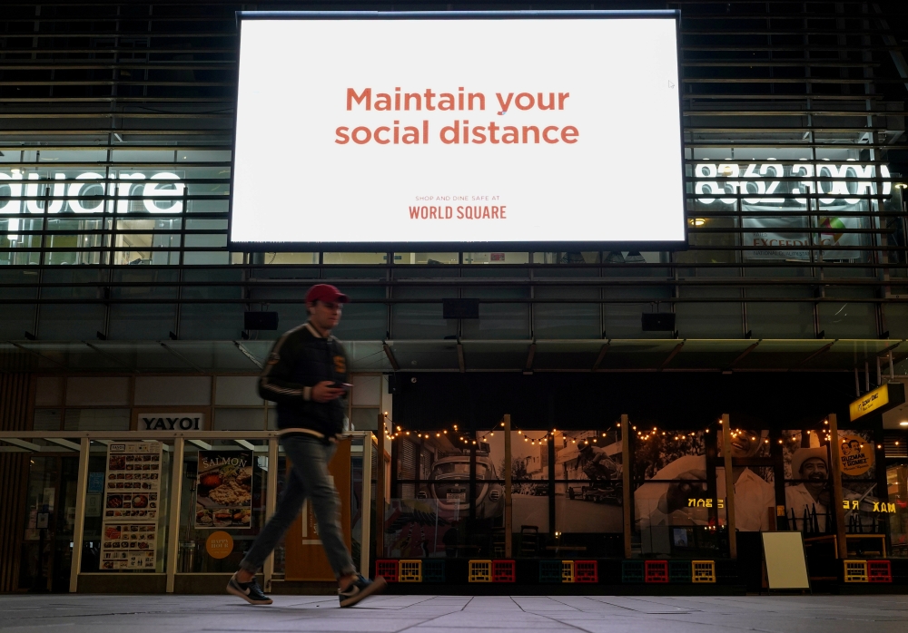 A man walks under a public health message about social distancing displayed at a shopping plaza in the city centre during a lockdown to curb the spread of a coronavirus disease (COVID-19) outbreak in Sydney, Australia, July 6, 2021. REUTERS/Loren Elliott/