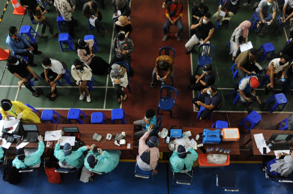 People wearing protective face masks sit before receiving the coronavirus disease (COVID-19) vaccine during the mass vaccination program for financial services industry at a school, as cases surge in Palembang, South Sumatra province, Indonesia July 13, 2