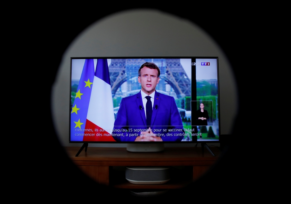 French President Emmanuel Macron is seen on a screen as he addresses the nation about the state of the coronavirus disease (COVID-19) outbreak, in Boulogne Billancourt, France, July 12, 2021. REUTERS/Gonzalo Fuentes
