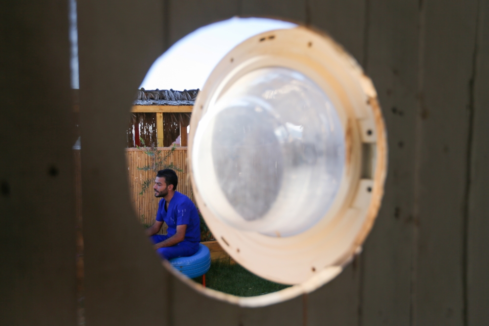 Palestinian artist, Ali Mhana, is seen through a glass door of a washing machine that he used as a window of a his makeshift office at an environment-friendly beachfront cafe in Gaza July 8, 2021. Picture taken July 8, 2021. REUTERS/Ibraheem Abu Mustafa