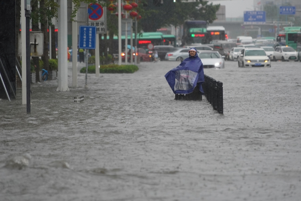 A resident wearing a rain cover stands on a flooded road in Zhengzhou, Henan province, China July 20, 2021. (cnsphoto via REUTERS)