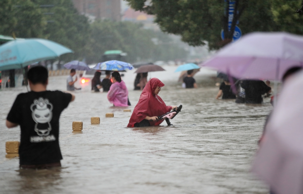 Residents wade through floodwaters on a flooded road amid heavy rainfall in Zhengzhou, Henan province, China July 20, 2021. (China Daily via REUTERS)