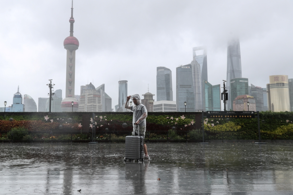 A man with luggage walks in the rain on The Bund as Typhoon In-fa approaches Shanghai, China July 25, 2021. cnsphoto via REUTERS