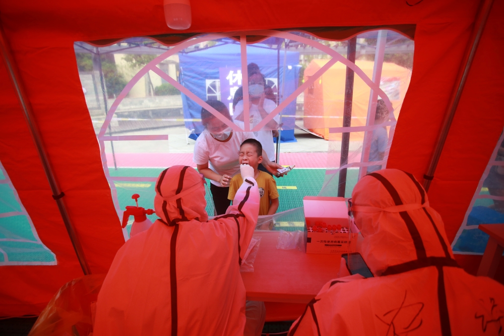 A medical worker collects a swab from a child for nucleic acid testing following the coronavirus disease (COVID-19) outbreak in Yangzhou, Jiangsu province, China August 9, 2021. China Daily via REUTERS