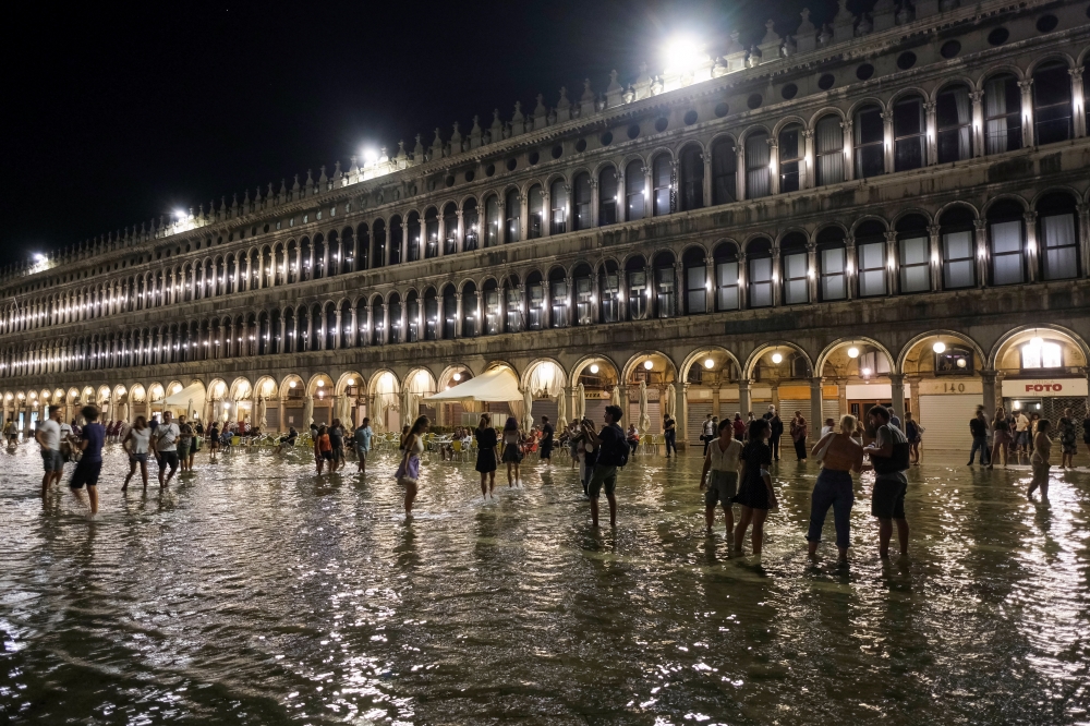 People walk in a flooded St. Mark's Square during an exceptional high water in Venice, Italy August 8, 2021. Picture taken August 8, 2021. REUTERS/Manuel Silvestri