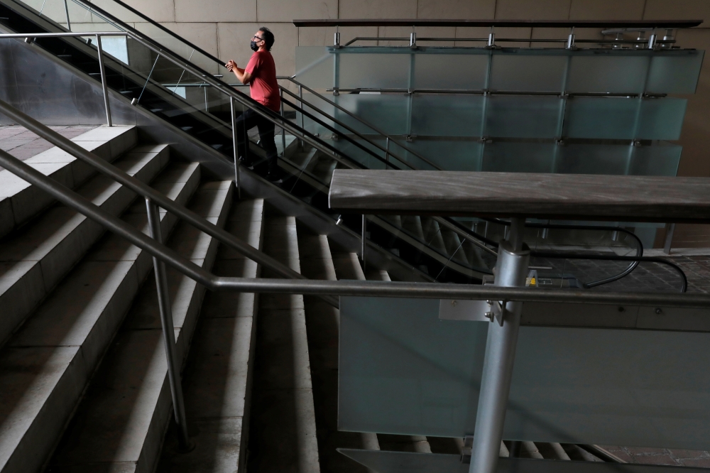 A person in a face mask rides an escalator in an otherwise empty pedestrian mall during the outbreak of the coronavirus disease (COVID-19) in the Downtown area of Manhattan, New York City, U.S., August 9, 2021. REUTERS/Andrew Kelly