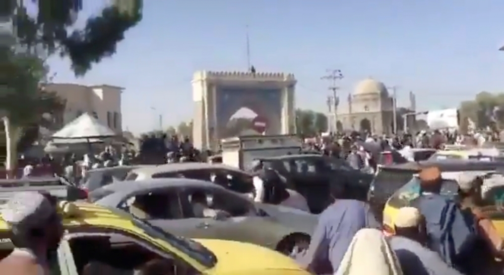 People and cars gather in the Eid Gah Darwaza area as a flag is hoisted on the Kandahar city gate, in Kandahar, Afghanistan in this screen grab taken from a handout video uploaded on social media August 14, 2021. Taliban Handout/via Reuters
