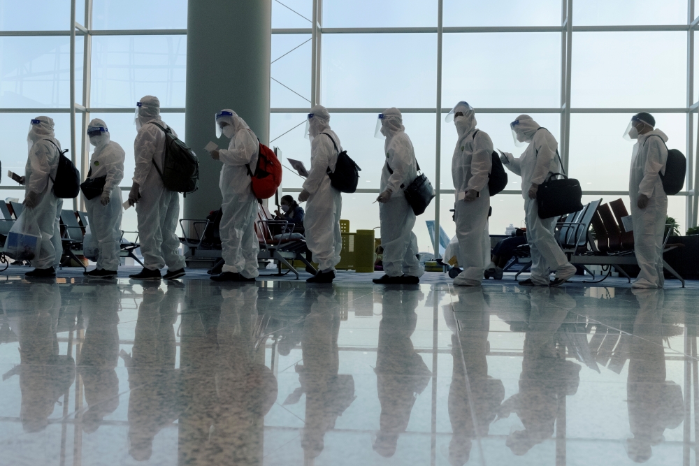 Passengers wearing protective suits (PPE) line up to board their plane for an international flight at Hong Kong airport amid the spread of the coronavirus disease (COVID-19), China July 9, 2021. REUTERS/Thomas Peter/File Photo