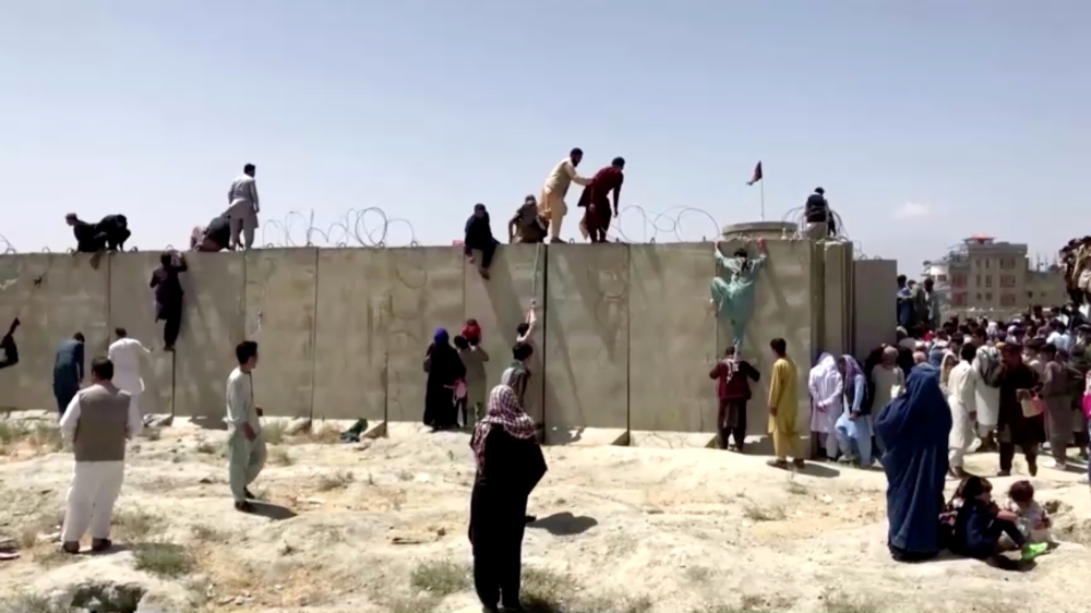 People climb a barbed wire wall to enter the airport in Kabul, Afghanistan August 16, 2021, in this still image taken from a video. Reuters TV/via Reuters/File Photo