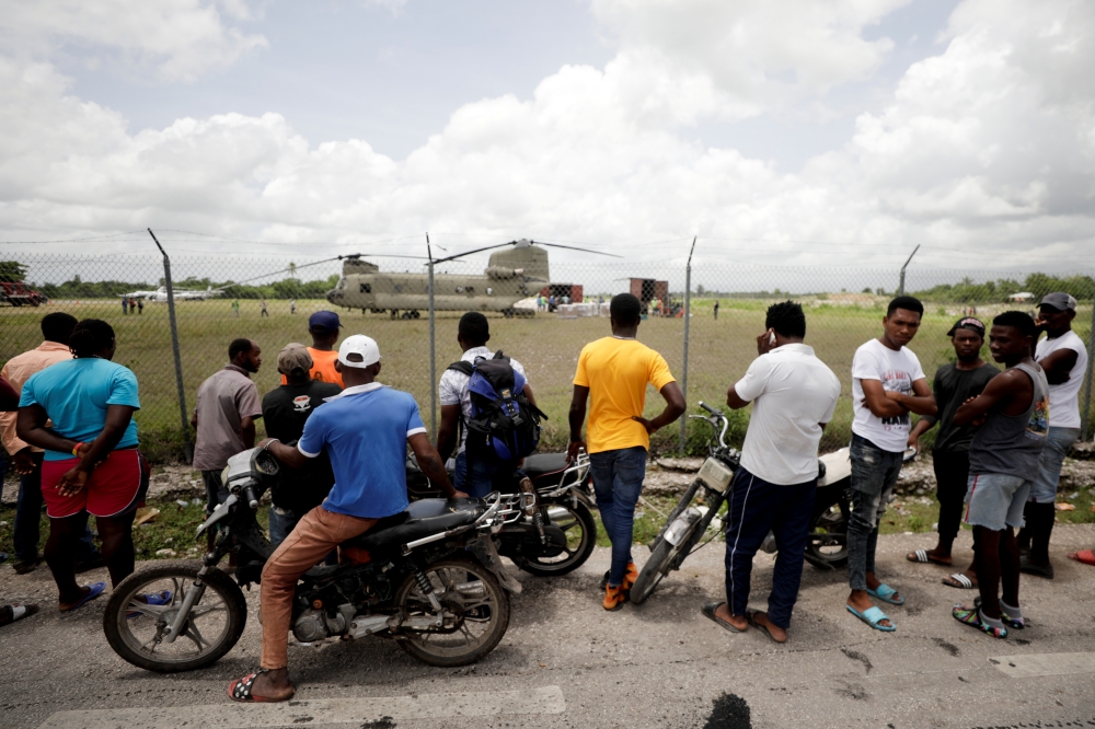 Residents look on as workers receive humanitarian aid from a U.S. military helicopter at Les Cayes airport after Saturday's 7.2 magnitude earthquake, in Les Cayes, Haiti, August 18, 2021. REUTERS/Henry Romero
