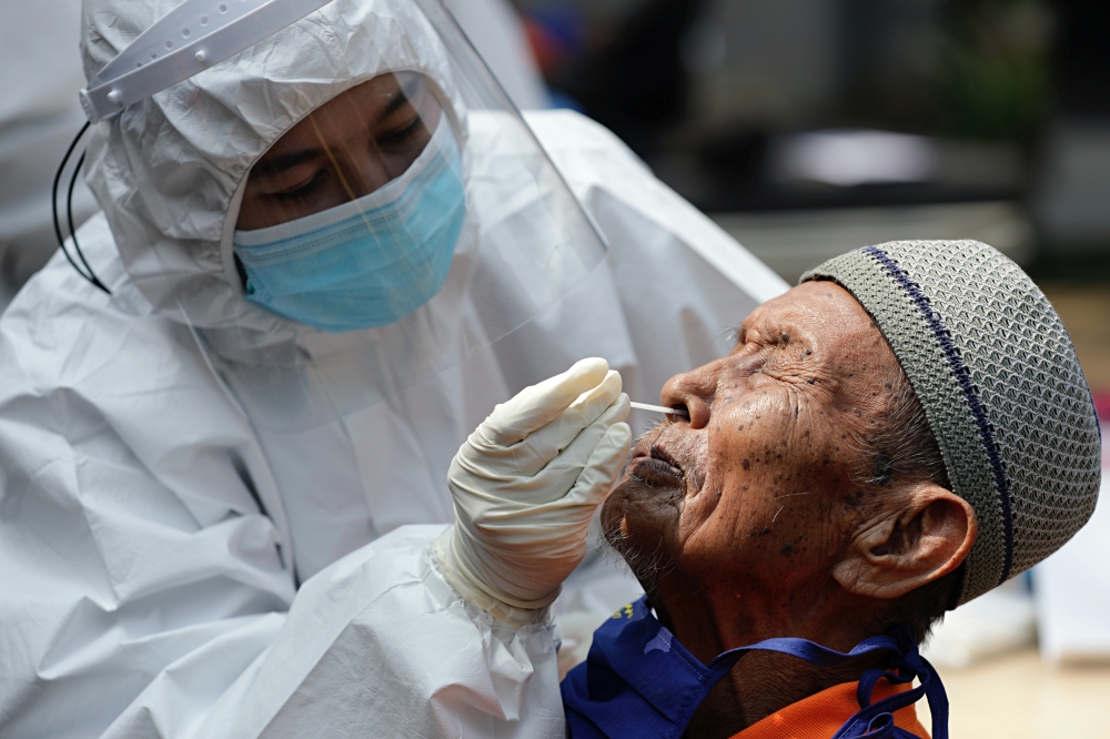 A healthcare worker wearing personal protective equipment suits (PPE) takes a swab sample from an elderly man with mental illness to test for the coronavirus disease (COVID-19) at a social home in Jakarta, Indonesia, August 23, 2021. REUTERS/Ajeng Dinar U