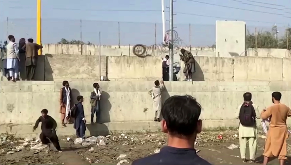 People stand on a barrier outside Kabul airport, Afghanistan, August 22, 2021 in this still image taken from video. REUTERS/ReutersTV