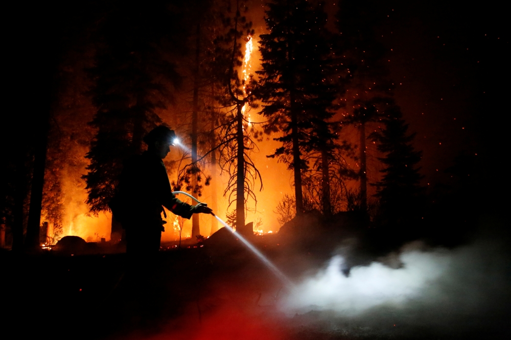 Patrick R., 27, a firefighter with Cal Fire sprays water on hot spots as flames from the Caldor Fire burn through trees in Christmas Valley near South Lake Tahoe, California, U.S., August 31, 2021. REUTERS/Brittany Hosea-Small