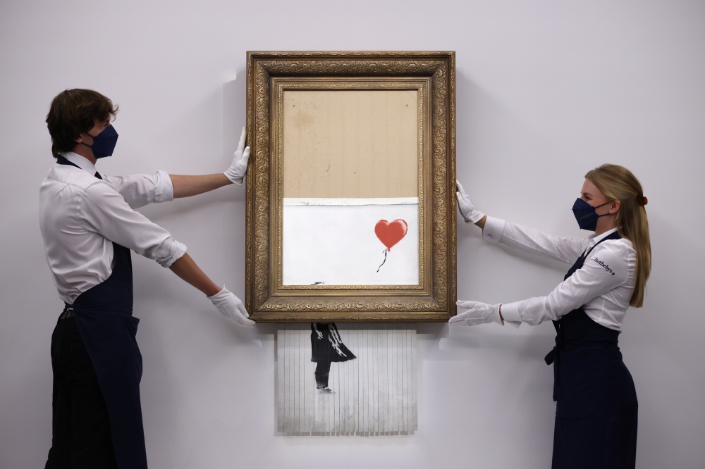 A gallery assistant poses by 'Love is in the Bin', an artwork by Banksy, which will be for sale in an auction, at Sotheby's in London, Britain, September 3, 2021. REUTERS/Tom Nicholson