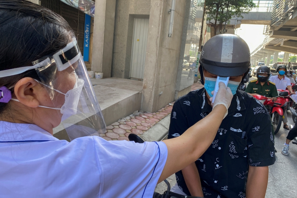 A health worker checks the temperture of a motorcycle driver at a check point during the first day of the extended lockdown in Hanoi, Vietnam, September 6, 2021. REUTERS/Stringer