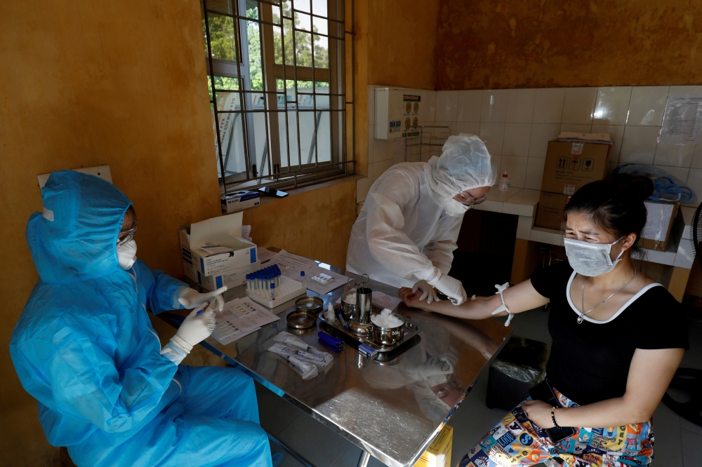 Medical specialists wearing protective suits collect blood sample from a woman who has returned after travelling to Da Nang, at a rapid testing center for coronavirus disease (COVID-19) outside Hanoi, Vietnam July 30, 2020. REUTERS/Kham/File Photo