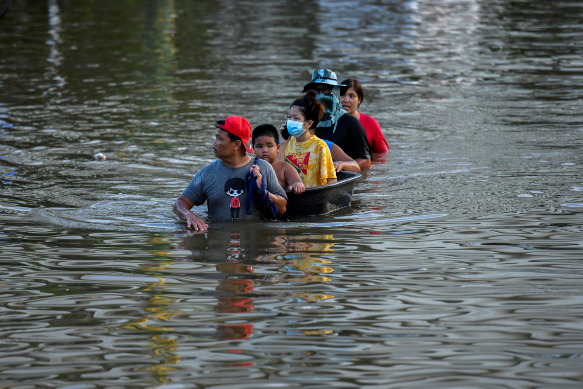 People sit on a makeshift boat as a man pulls it through a flooded street in Chaiyaphum province, Thailand, September 28, 2021. REUTERS/Panumas Sanguanwong