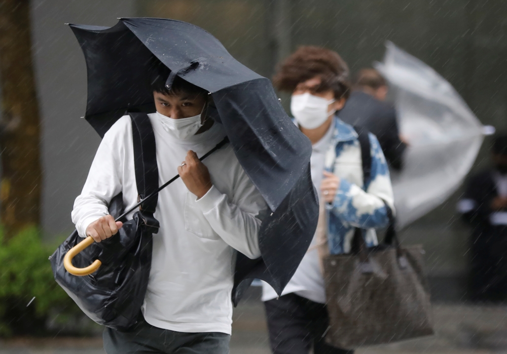 Men wearing protective masks amid the coronavirus disease (COVID-19) outbreak, make their way in the heavy rain caused by Typhoon Mindulle in Tokyo, Japan, October 1, 2021. REUTERS/Kim Kyung-Hoon