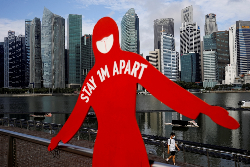 A man wearing a face mask passes a sign put up to encourage social distancing during the coronavirus disease (COVID-19) outbreak, at Marina Bay in Singapore, September 22, 2021. Reuters/Edgar Su/File Photo