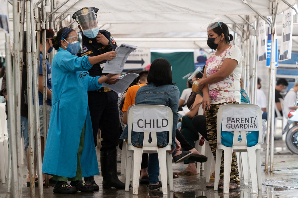 A health worker checks the documents of a child scheduled to be inoculated with Pfizer-BioNTech vaccine against the coronavirus disease (COVID-19), during the vaccine rollout for children with comorbidities, in Pasig, Metro Manila, Philippines, October 15