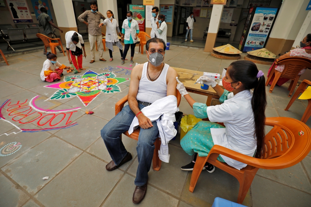 A healthcare worker gives a dose of the COVISHIELD vaccine against the coronavirus disease (Covid-19), manufactured by Serum Institute of India, to a man as others decorate the vaccination centre to celebrate the milestone of administering one billion COV