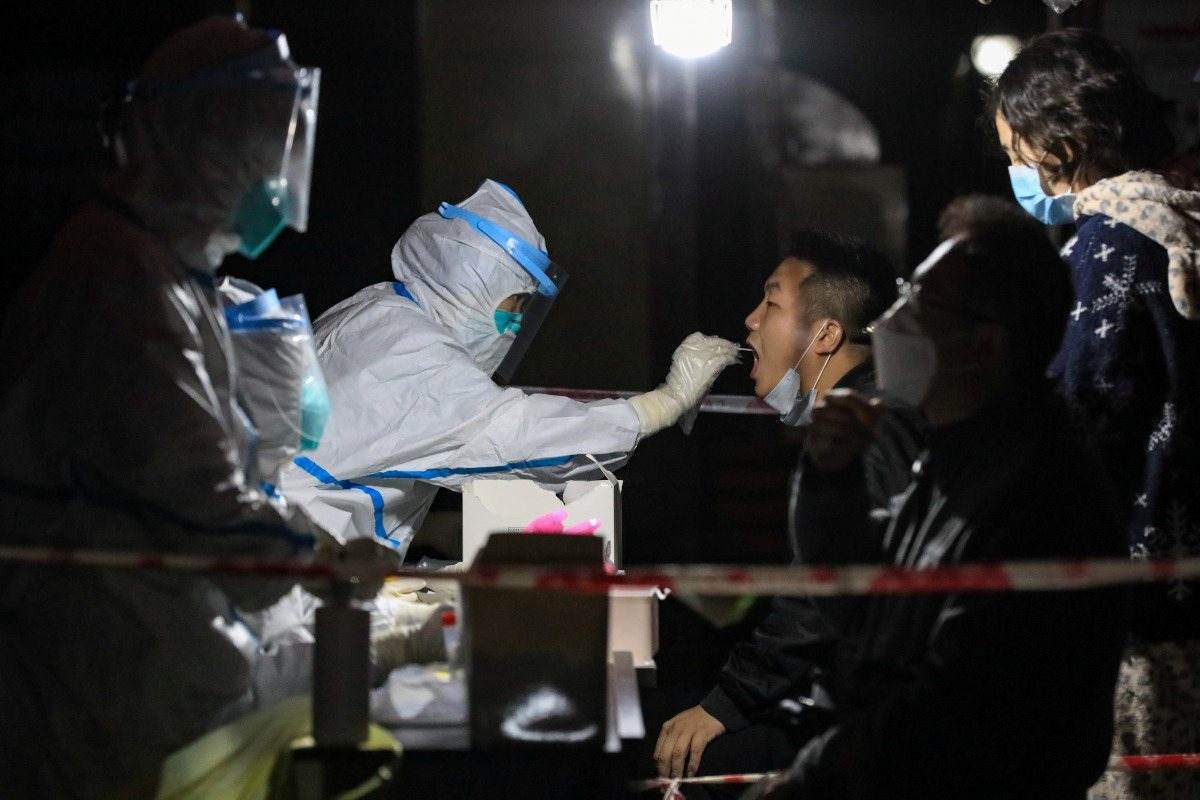 A medical worker in protective suit collects a swab from a resident at a makeshift nucleic acid testing site inside a residential compound, following new cases of the coronavirus disease (COVID-19), in Zunyi, Guizhou province, China October 21, 2021. Pict