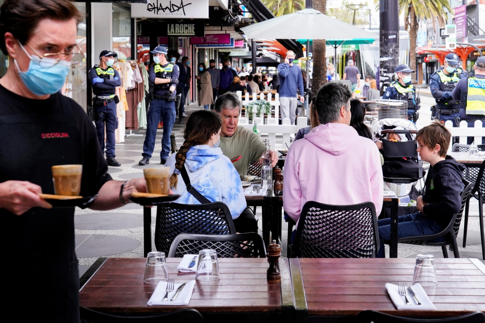 Diners eat outside a cafe in St Kilda while police stand by due to a Victorian Freedom Movement protest on the second day of eased coronavirus disease (COVID-19) regulations in Melbourne, Australia, October 23, 2021. Reuters/Sandra Sanders