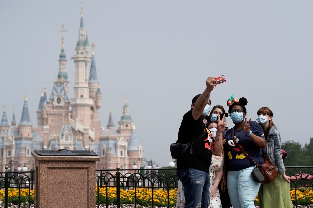 Visitors wearing protective face masks pose for a picture at Shanghai Disney Resort. Reuters/Aly Song/File Photo