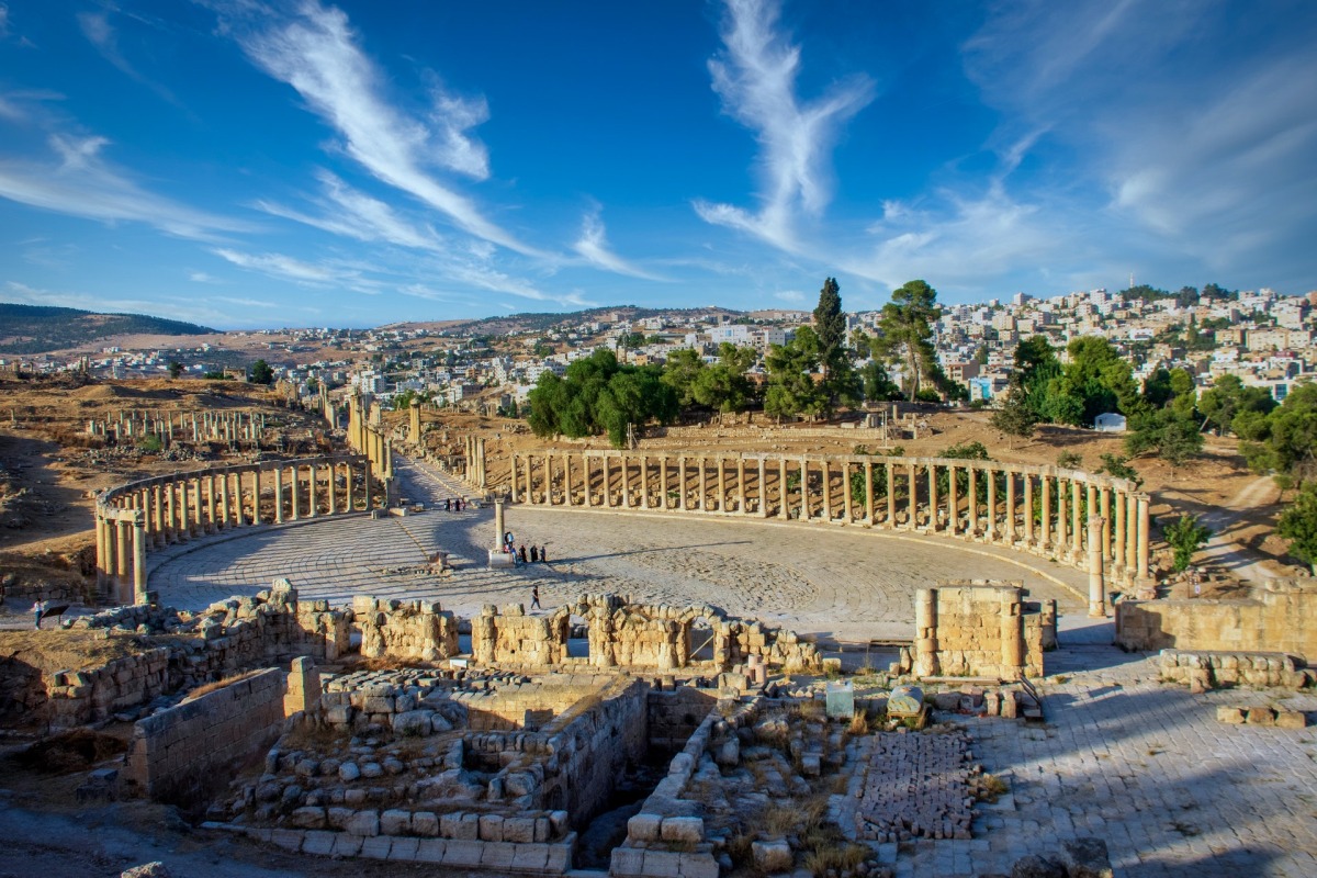 Oval Forum and long colonnaded street or cardo ancient Greco-Roman city Gerasa. Modern Jerash on background.