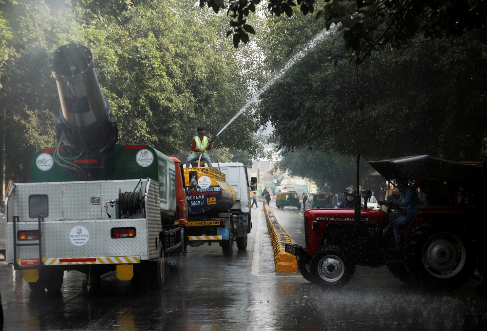 A vehicle with an anti smog gun passes by as a labourer sprinkles water using a tanker to settle dust and to curb air pollution in New Delhi, India, November 8, 2021. REUTERS/Anushree Fadnavis