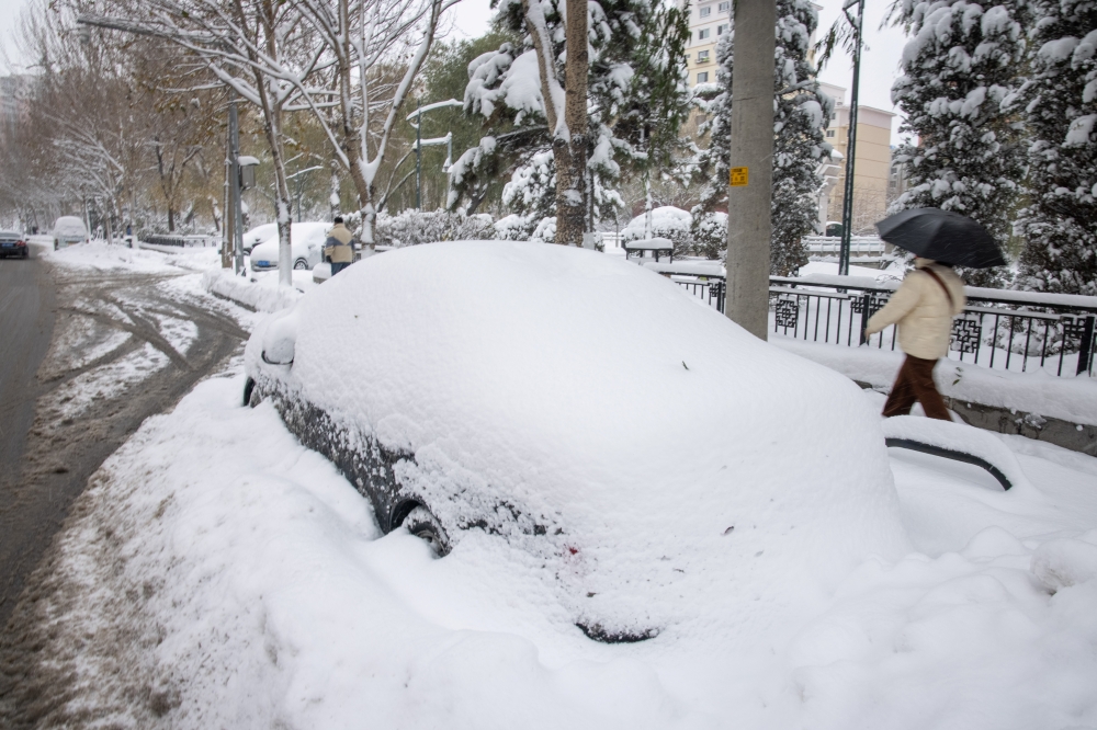 People walk past a car covered in snow following heavy snowfall in Shenyang, Liaoning province, China November 9, 2021. Picture taken November 9, 2021. China Daily via REUTERS