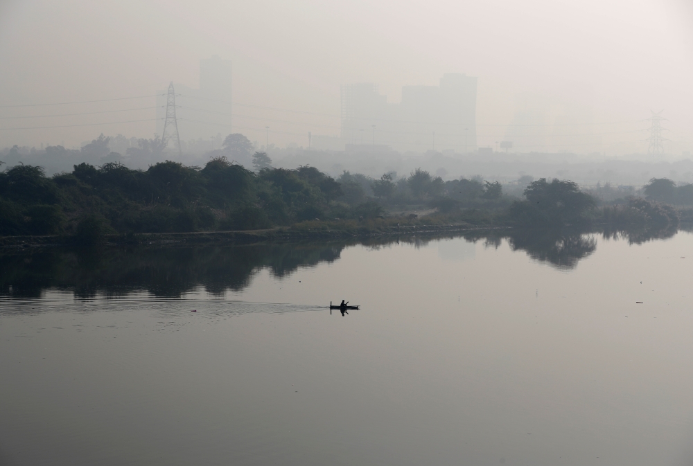 A man rows a boat as buildings shrouded in smog are seen in the background on the outskirts of Delhi, India, November 15, 2021. REUTERS/Adnan Abidi