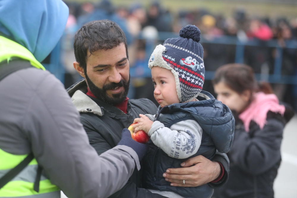 A child holds an apple during the distribution of humanitarian aid among migrants near Bruzgi - Kuznica checkpoint on the Belarusian-Polish border in the Grodno region, Belarus November 17, 2021. Leonid Scheglov/BelTA