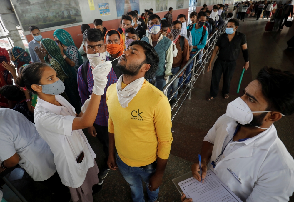A healthcare worker collects a swab sample from a passenger as others wait for their turn upon arrival at a railway station during a rapid antigen testing drive for the coronavirus disease (COVID-19) in Ahmedabad, India, November 30, 2021. REUTERS/Amit Dave