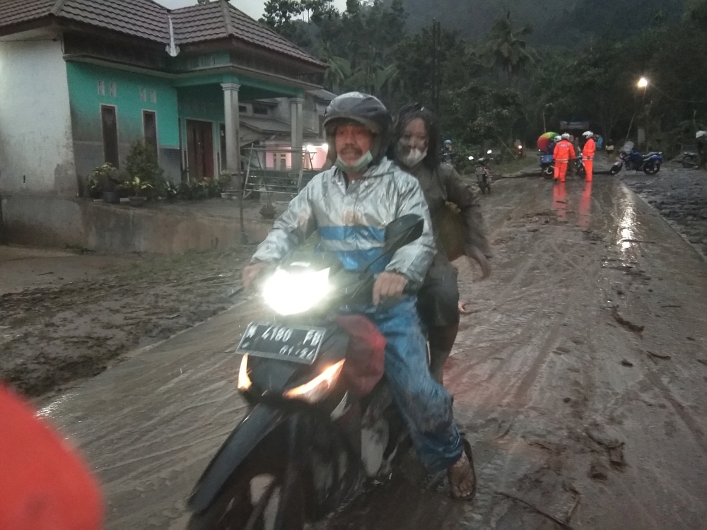 People ride a motorbike on a road that is covered with volcanic ash following an eruption of the Semeru mount volcano at Sumberwuluh village in Lumajang regency, East Java province, Indonesia, December 4, 2021, in this photo taken by Antara Foto. Antara Foto/Hermawan/via REUTERS