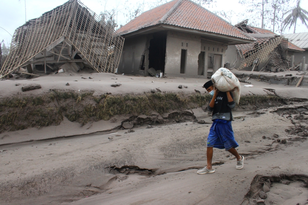 A villager carries his belongings during an evacuation following the eruption of Semeru mount volcano in Supiturang village, Lumajang, East Java province, Indonesia December 5, 2021, in this photo taken by Antara Foto/Ari Bowo Sucipto/via REUTERS