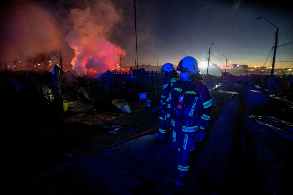 Firefighters walk amidst remains of houses which were burned following the spread of a wildfire in Castro area, in Chiloe, Chile, December 10, 2021. REUTERS/Alvaro Vidal