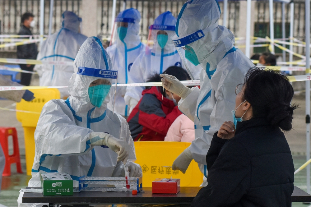 Medical workers in protective suits collect swabs from residents at a nucleic acid testing site during a third round of mass testing for the coronavirus disease (COVID-19) in Zhenhai district of Ningbo, Zhejiang province, China December 12, 2021. cnsphoto via REUTERS