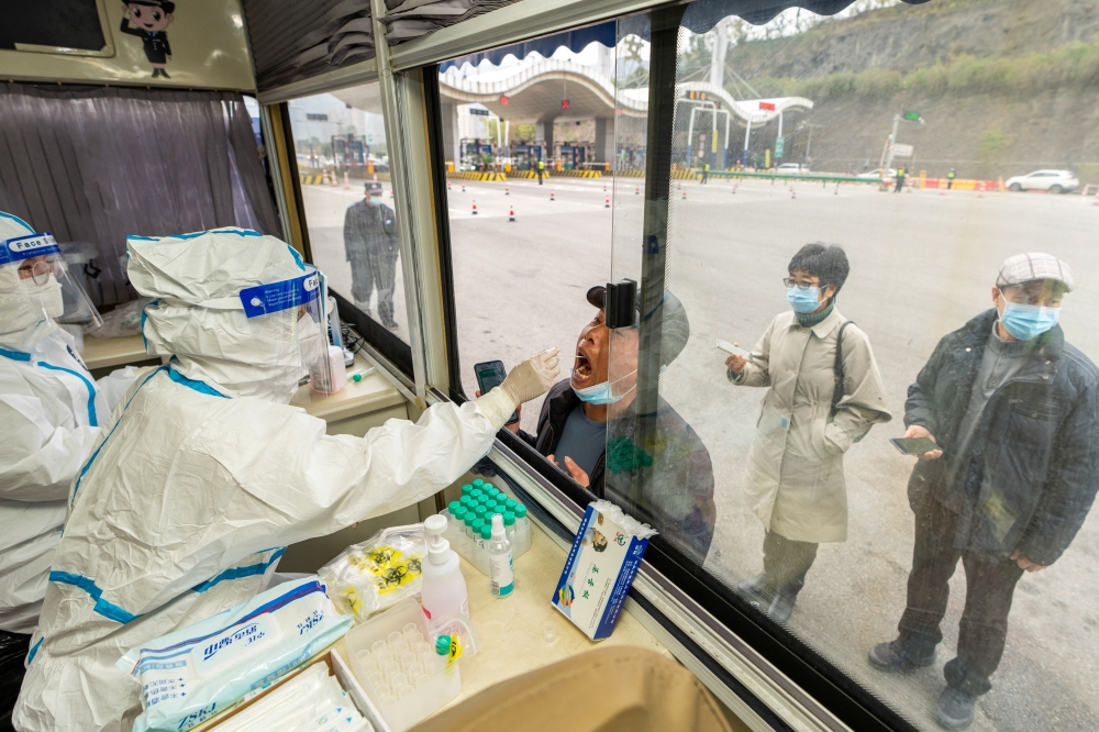 A medical worker in protective suit collects a swab from a man at a nucleic acid testing booth set up at a highway exit, following cases of the coronavirus disease (COVID-19) in the cities of Ningbo, Shaoxing and Hangzhou, in Ruian, Zhejiang province, China December 14, 2021. cnsphoto via REUTERS 