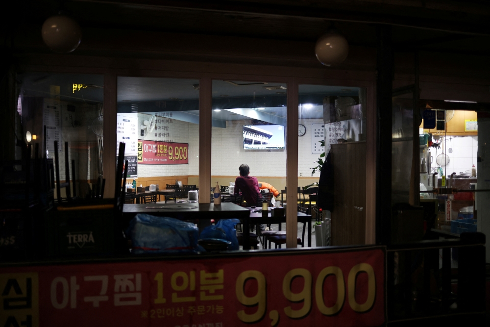 A restaurant owner watches a news report after closing his restaurant earlier, as part of tightened social distancing rules to contain a surge in coronavirus disease (COVID-19) infections, in Seoul, South Korea, December 20, 2021. REUTERS/Kim Hong-Ji